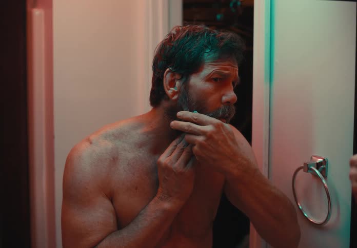 Shirtless man clipping his beard with small scissors in bathroom