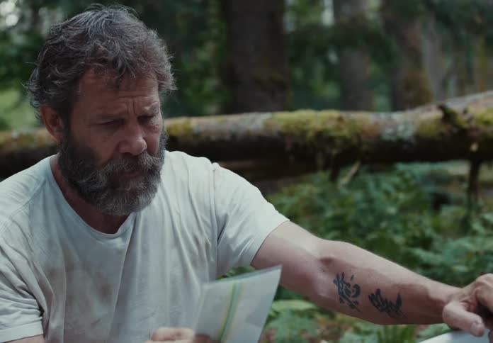 Middle aged man with a beard and a white shirt looks at a photograph with sadness and longing in the forest