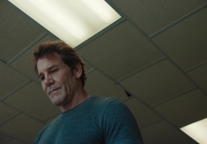 An older white man stands in a building and looks down