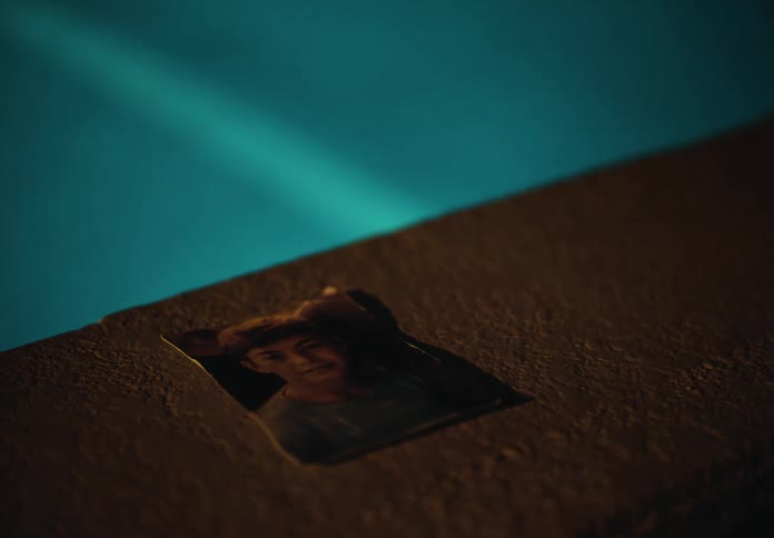 Person places torn photograph on concrete bordering blue pool water