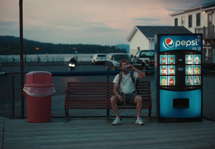 Man sitting next to soda machine drinking a soda at sunset