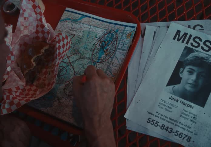 Man with missing person signs eats a hamburger while marking places in a map with a pen