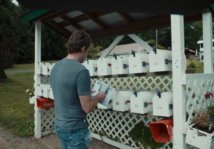 A man putting flyers into mailboxes with houses and trees in the background
