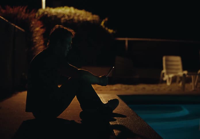 Man sits near edge of swimming pool contemplating paper