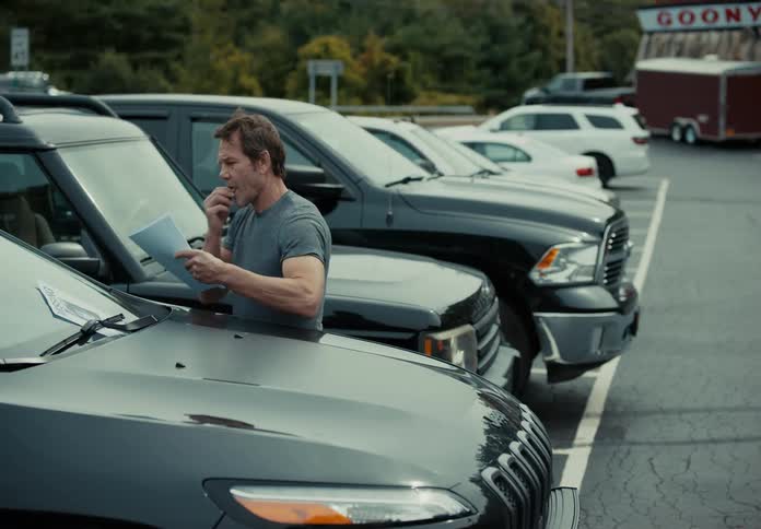 Man placing flyers on windshield of vehicles in a parking lot