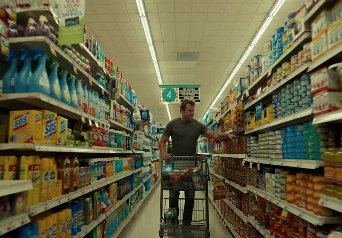 A man takes items off a shelf in a grocery store and puts them in his cart