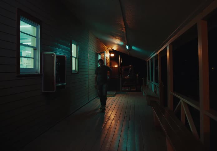 Man comes out to the wooden porch of a building to use a public payphone at night