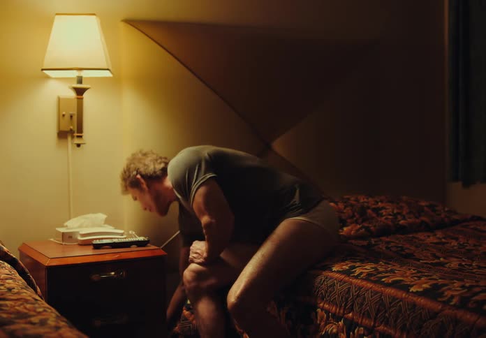 Man sits on bed in hotel room contemplating phone before turning off lamp