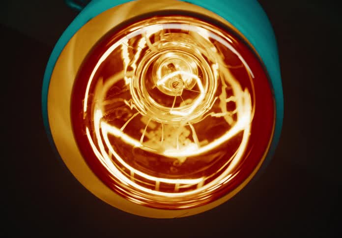 Close up of an incandescent light bulb turning on inside a lamp