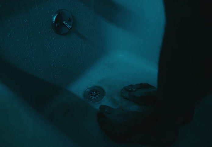 Person takes a shower in a dark bathroom cleaning dirt or blood from its feet