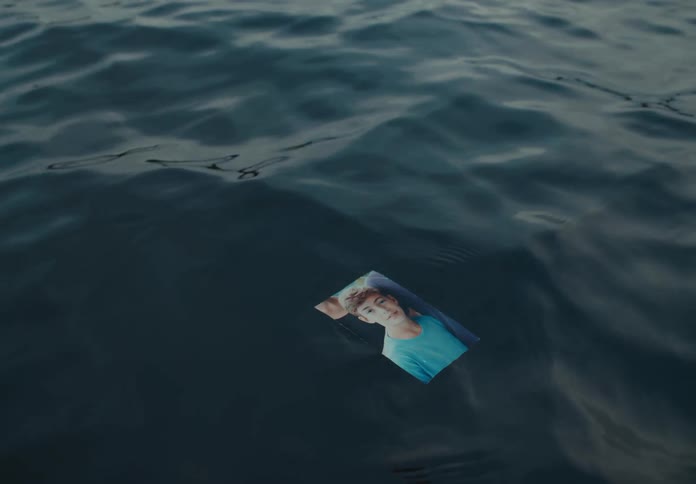 A man places a photo of a young boy in the ocean that briefly floats before falling in the water
