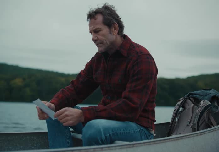 Man with black red striped shirt sitting in a boat looks at a photograph on a lake
