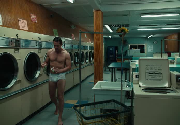 Man in his underwear walks up to a coin machine in a laundromat