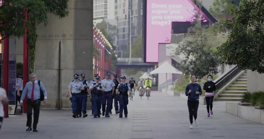 A city square with people walking jogging and riding bikes with buildings in the background