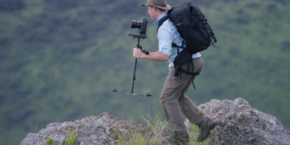 A photographer climbing up rocks to the side of a cliff
