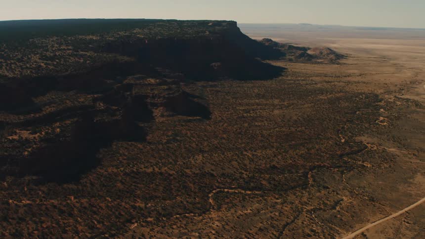 Dirt road winds through plains near cliff toward desert and mountains on horizon