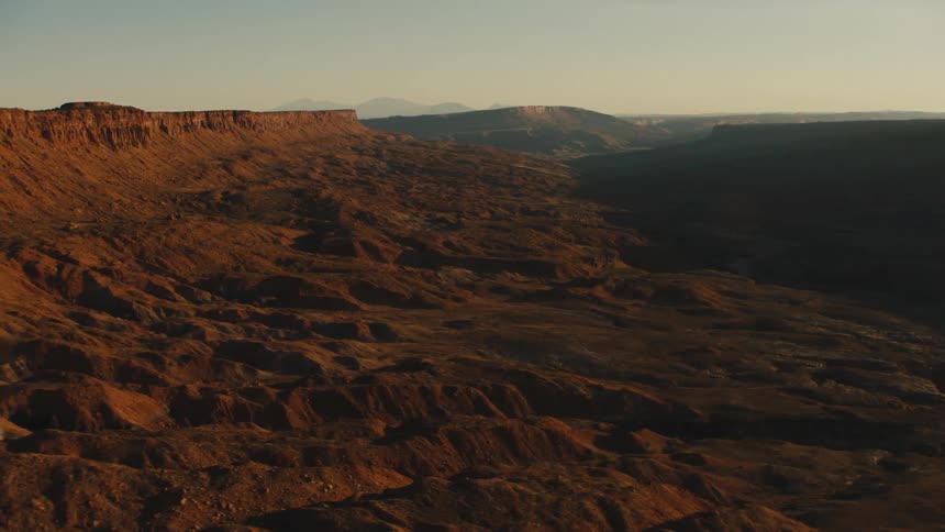 Sun cast shadows on rough terrain leading to wide plateau in badlands