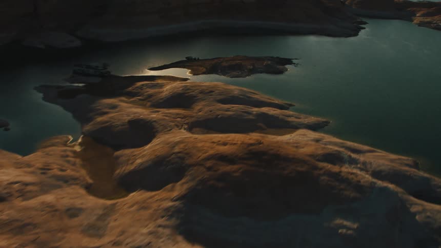 Water winding around flat stone terrain reflects sunlight
