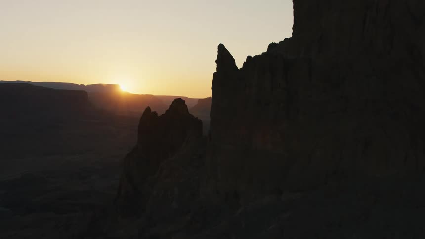 Sun sits on horizon as mesa and craggy peaks stand in shadows