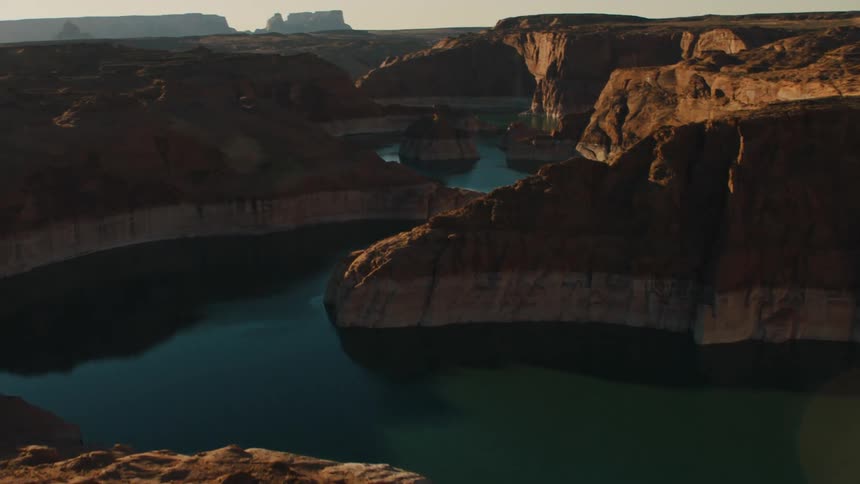 A rainbow shines in the sky as sunlight washes over a canyon with a blue river