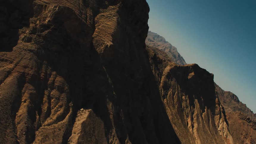Sun creates shadows under overhangs and crevices of sheer cliffside of mountain