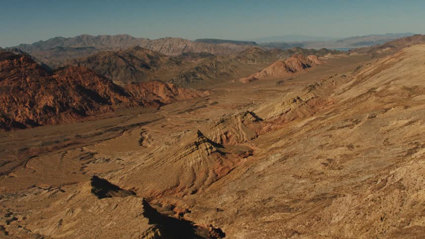 A desert with cliffs and mountains with the sky and clouds in the background