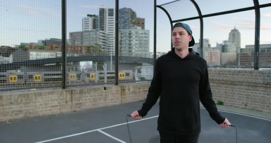 A man jumps rope on a rooftop in the city as a train passes behind him