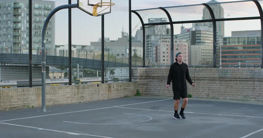 A man jumping rope on an outdoors basketball court in a metropolis during the day