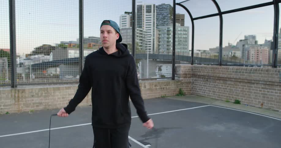 Man with a black hoodie and a cap jumps rope on the rooftop of a building