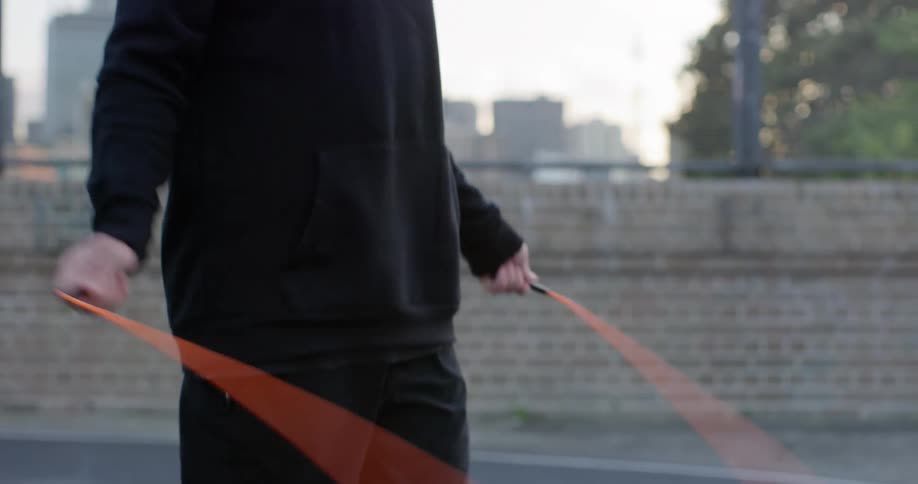 Man with a black hoodie jumps orange rope on the rooftop of a building at dusk
