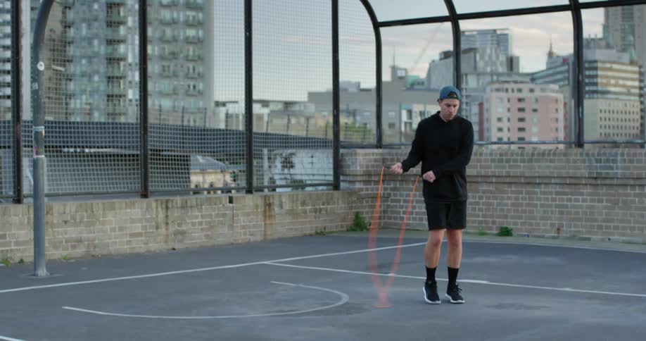 Man jumping rope on outdoor basketball court in city