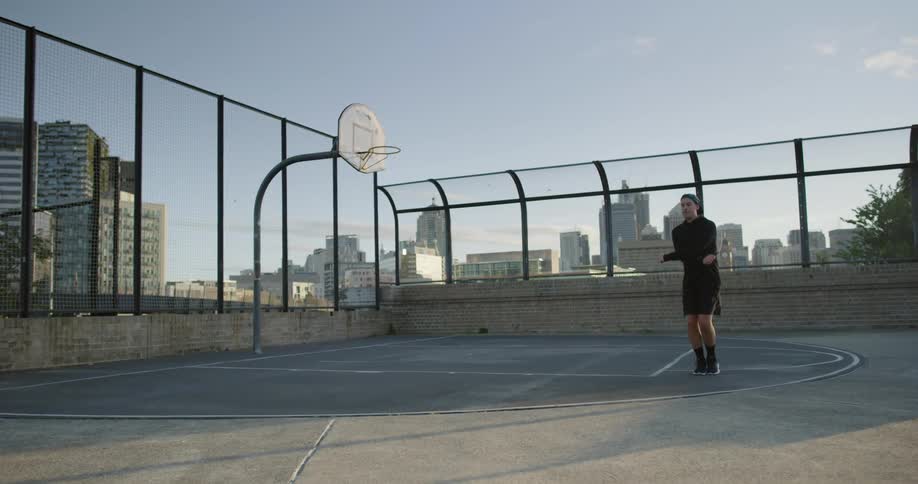 Man jumping rope in a basketball court in the city at sunset