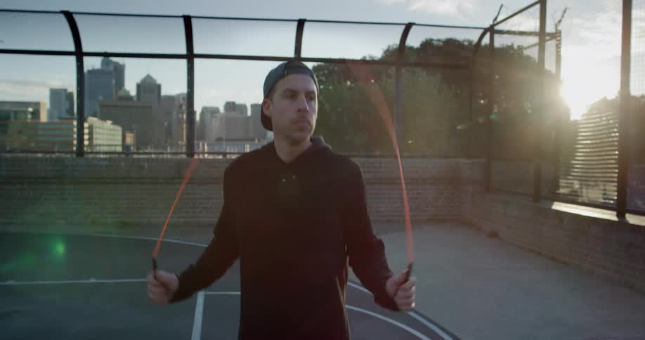 Man jumping rope on a basketball court in the city at sunset