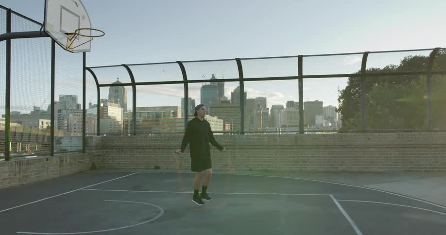 Man rope jumping in a basketball court in the city at sunset