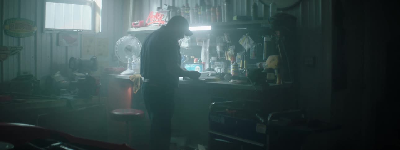 A mechanic walks through a garage to a bench and picks up paperwork