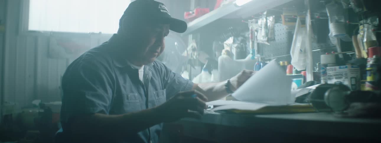 A mechanic sits at a bench and looks at paperwork