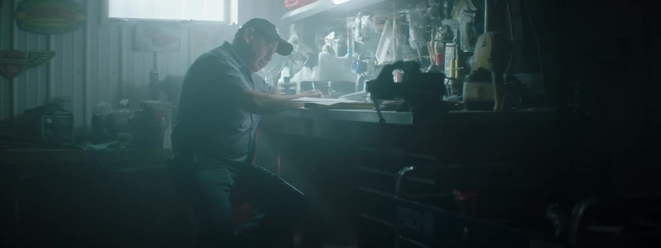 A man sitting on a stool is studying from a book in his garage during the day