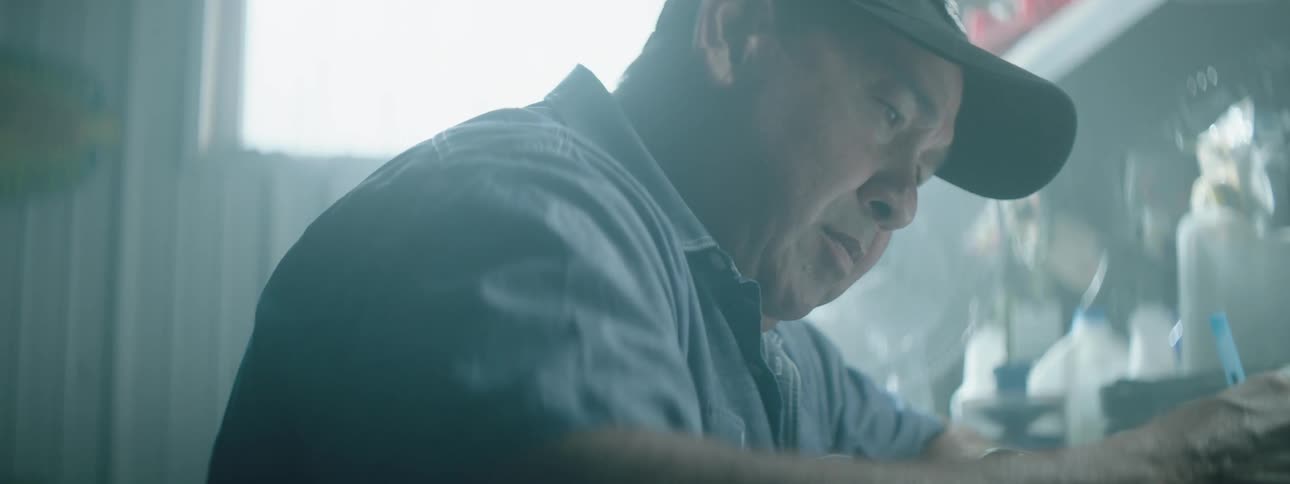 A man sits at a small space and uses a pen to write