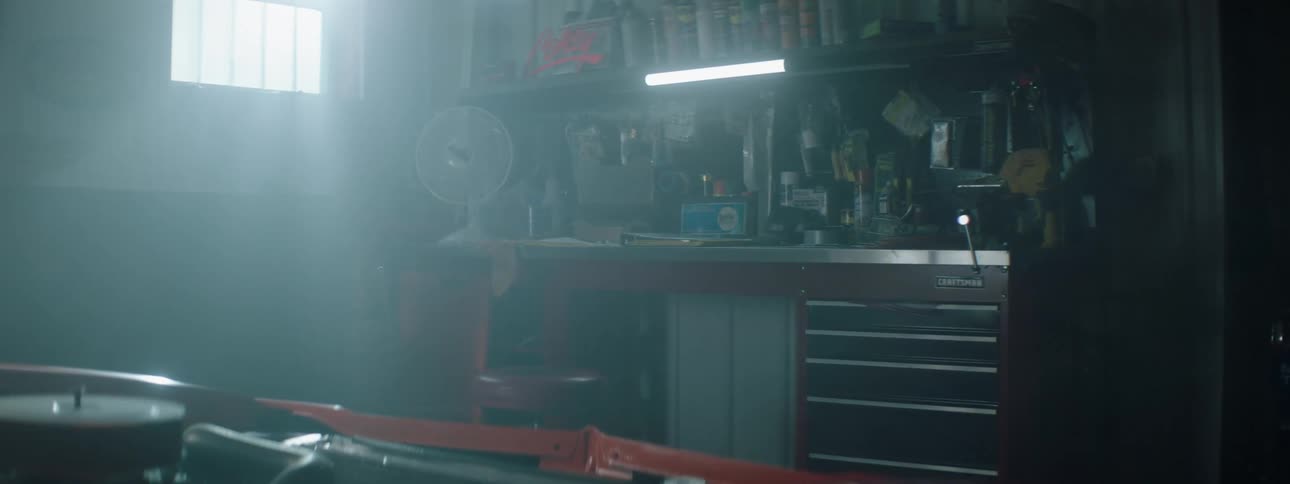 Sun shines through window into garage onto car engine and workbench