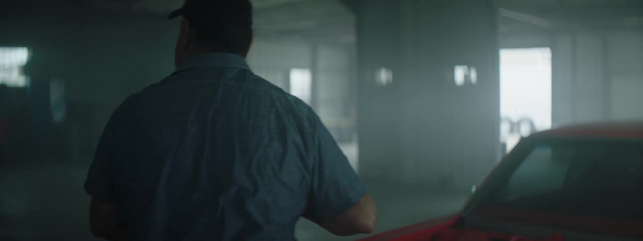 A man stands near a red car in a garage