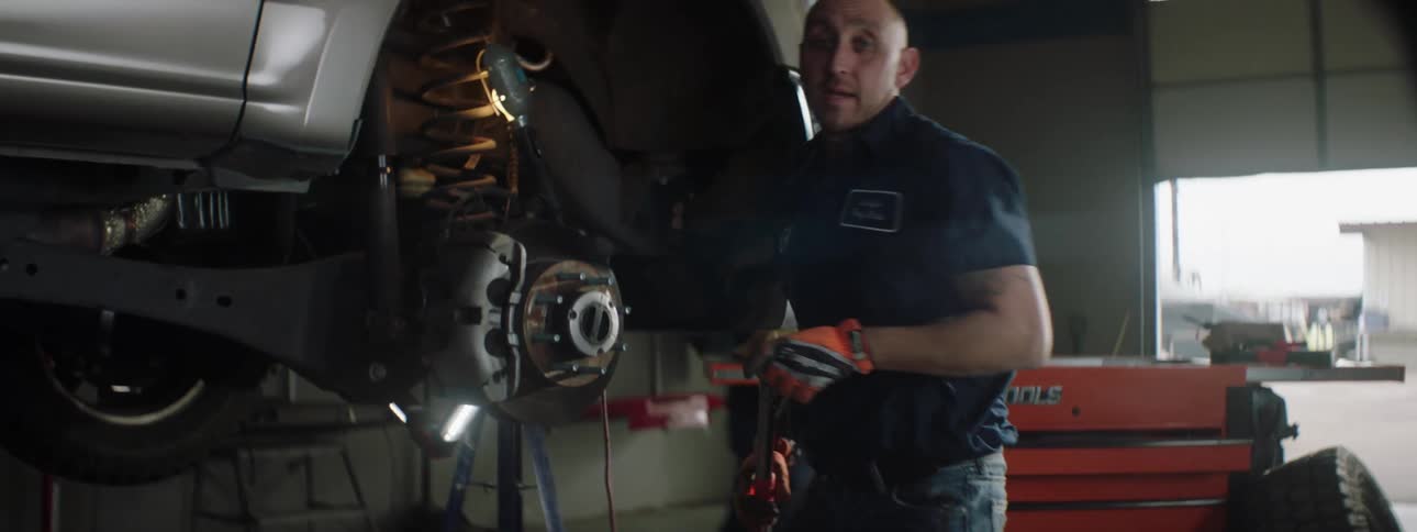 A mechanic works on a car as other mechanics walk past