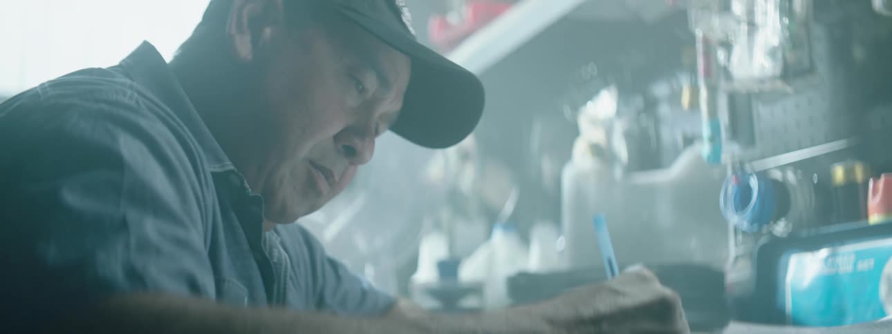 Man wearing baseball cap writes notes on a desk in a workshop