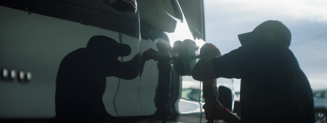 A mechanic uses a buffing tool on a pickup truck
