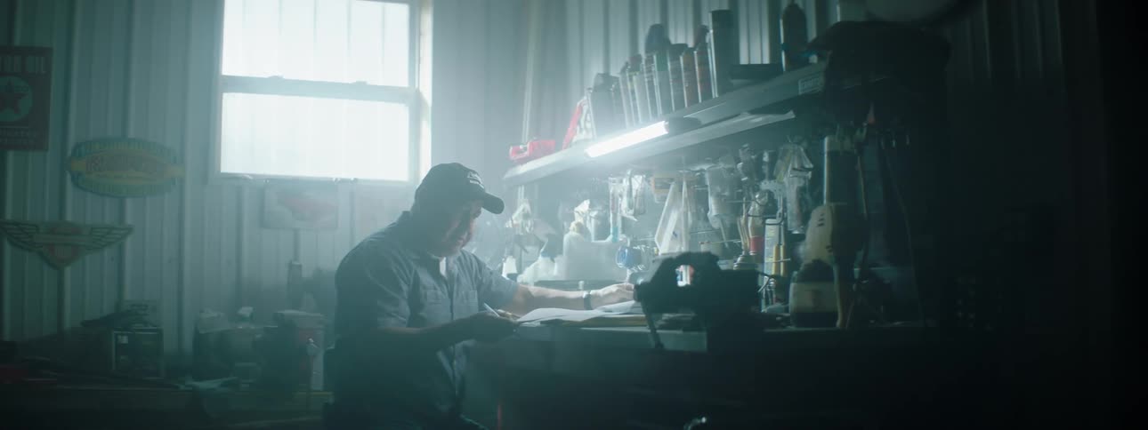 A man sits in a dark garage looking at papers on a desk