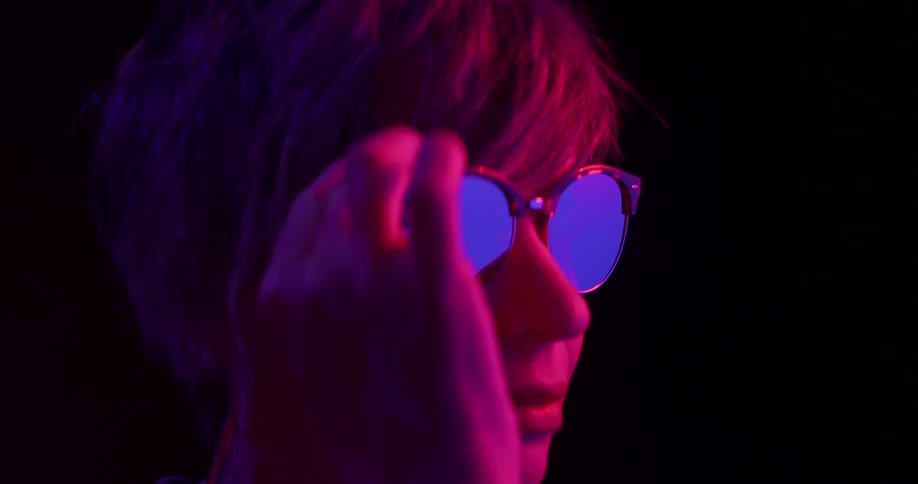 Woman reaches up to remove glasses under purple tinted lights