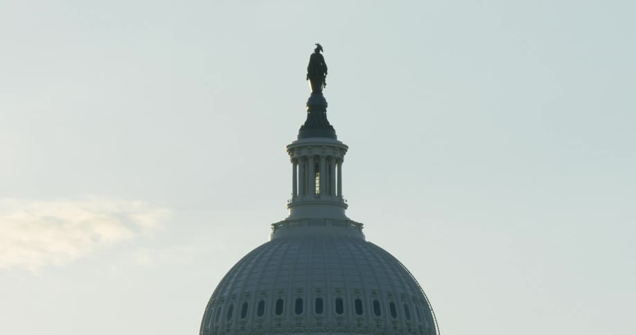 Statue and tower top dome of building under lightly clouded blue sky