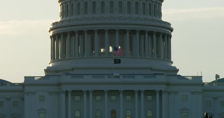 The american flag with a pow mia flag below it wave in the wind on the capitol building