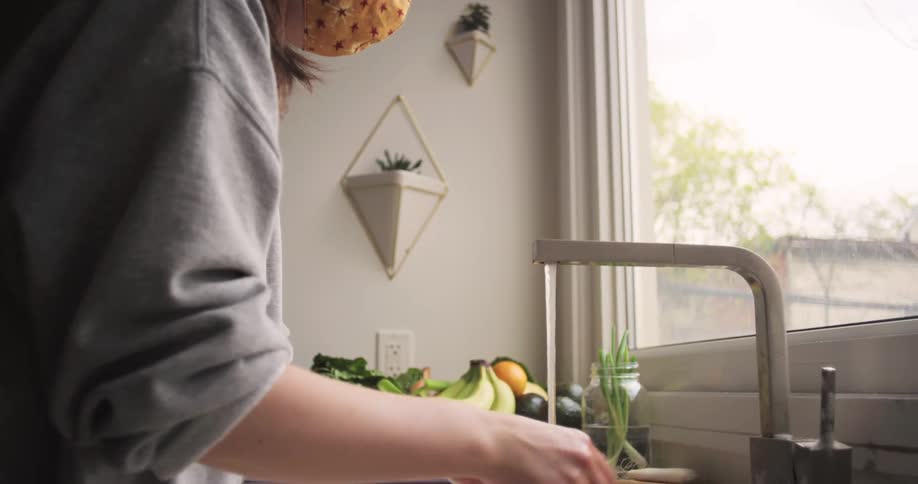 A young woman washes fruit in her kitchen sink