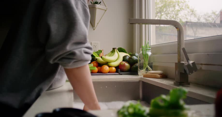 Woman washing then snipping fresh produce at the kitchen sink