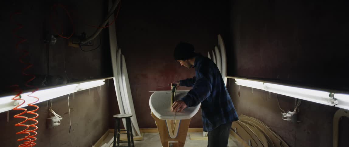Man working in one person surfboard manufacturing shop measures board